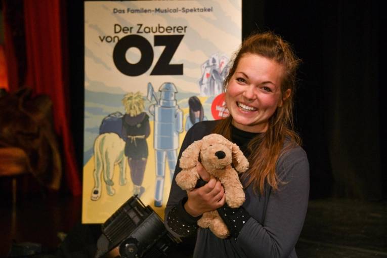 Viktoria Weiner mit einem Plüschtier in den Händen vor einem Plakat zum Musical "Der Zauberer von Oz".